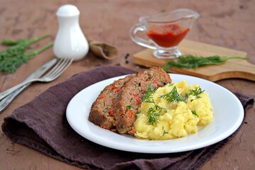 A meatloaf with mushrooms and red sweet pepper on a white plate with a garnish of mashed potatoes.
