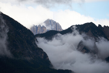 Dramatic dolomite rock between clouds with green forest below