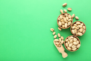 Fototapeta na wymiar Tasty pistachios in bowls and scoop on green background