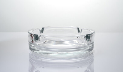 Transparent glass ashtray on a glossy light background. Side view.