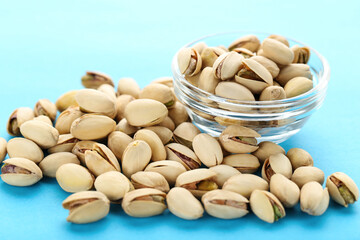 Tasty pistachios in bowl on blue background