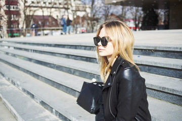 Fototapeta premium Blonde girl in sunglasses and a leather jacket on the street in the city