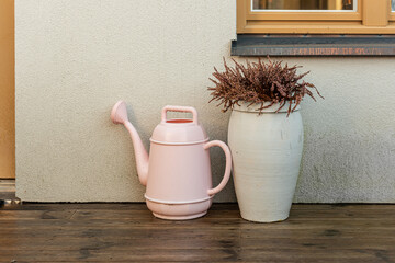 Watering can and a pot with heather by a house.