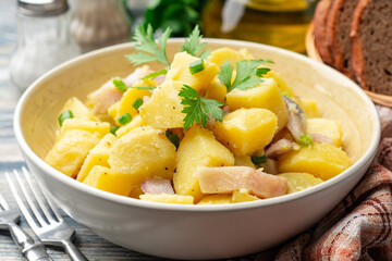 Potato salad with salted herring, onion and parsley in bowl on rustic wooden table