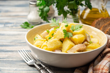 Potato salad with salted herring, onion and parsley in bowl on rustic wooden table