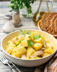 Potato salad with salted herring, onion and parsley in bowl on rustic wooden table