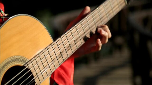 A musician in a red shirt plays the guitar outdoors