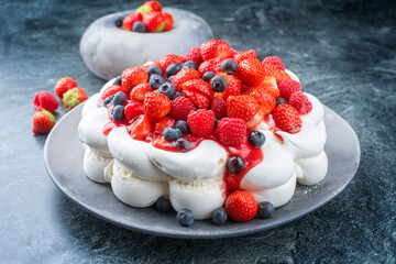 Modern style traditional Australian Pavlova torte with meringue cream and fruits offered as close-up on design plate with copy space