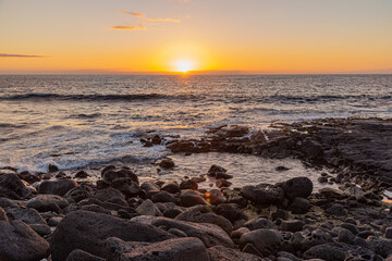 Fototapeta na wymiar Tropical orange sunset over lava rock shoreline and ocean