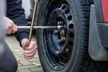 A wrench in the hands of an auto mechanic unscrews the bolts and nuts of a car wheel. Seasonal...