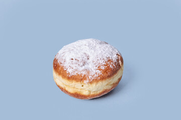 The view from the top. Delicious doughnut with filling, sprinkled with powdered sugar. Isolated on a blue background. High-calorie food.
