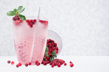 Fresh beverage berry drink with red lingonberry and green leaves in sunbeam on white wooden board, copy space.