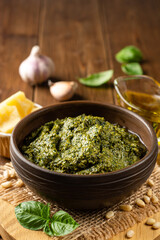 Homemade pesto sauce in ceramic bowl and ingredients on wooden background