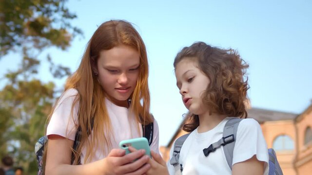 Portrait of cheerful preteen girls using smartphone standing outdoors