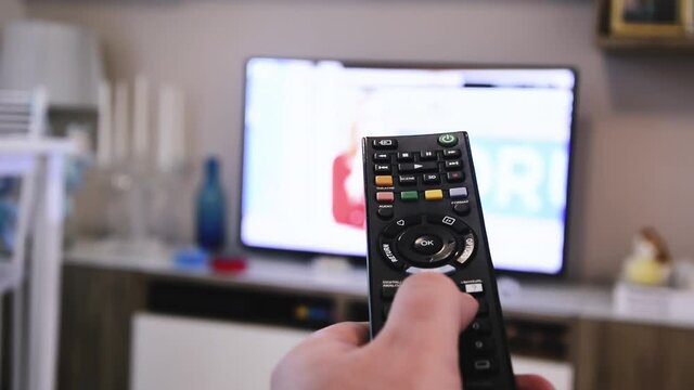 a male hand holds a remote control pushing the buttons to change the television channel
