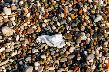 Dirty used disposable medical face mask on a pebble beach by sea. Waste during COVID-19. Pollution due coronavirus pandemic