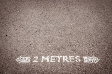 Fototapeta premium Social distancing road painted sign recommending staying 2 metres apart