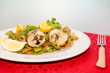 Merluza a la plancha con verduras, sobre mantel rojo y fondo blanco.