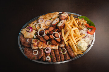 several types of roasted meat served on an oval, Serbian dish 