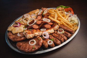 several types of roasted meat served on an oval, Serbian dish 