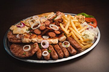 several types of roasted meat served on an oval, Serbian dish 