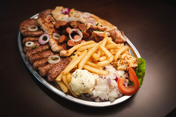 several types of roasted meat served on an oval, Serbian dish 