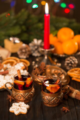 Glasses of mulled wine with cinnamon, tangerines and gingerbread on a background of candles, lights. Christmas, New Year's  idea, concept