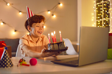 Happy boy sitting at laptop computer and having online birthday party with friends or relatives
