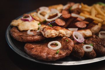 several types of roasted meat served on an oval, Serbian dish 