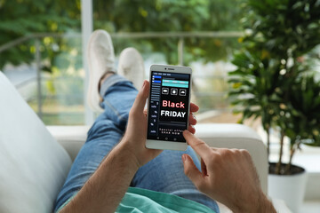 Man shopping online using smartphone on couch at home, closeup. Black Friday Sale
