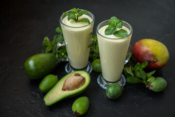 Two glasses of fruit smoothie from mango, avocado, feijoa and cream on a dark background