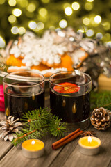 Two glasses of mulled wine with cinnamon and anise on a wooden background with fir branches and candles. Winter Christmas still life, beautiful bokeh, postcard.
