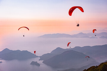 Paragliding in the sky. Paraglider tandem flying over the sea with mountains at sunset. Aerial view...