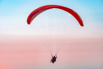 Paragliding in the sky. Paraglider tandem flying over the sea with mountains at sunset. Aerial view...