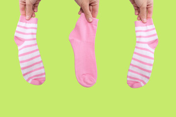 Hand holding three socks in pink color gamma from white to pink close up on green background