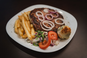 baked barbecue with french fries and salad and onion on a plate, Serbian dish 