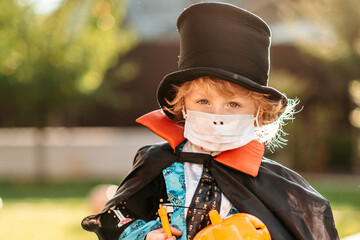 Happy Halloween. A child in a medical mask in a dracula costume sits on a pumpkin in his yard.