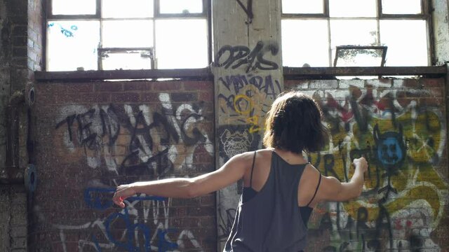 Woman Practicing Dance Moves In A Warehouse With Graffiti Filled Walls - medium shot