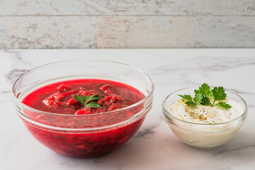 Beet soup and sour cream with fresh cilantro close up in a glass bowls on marble background