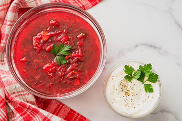 Beet soup and sour cream with fresh cilantro close up in a glass bowls on marble background