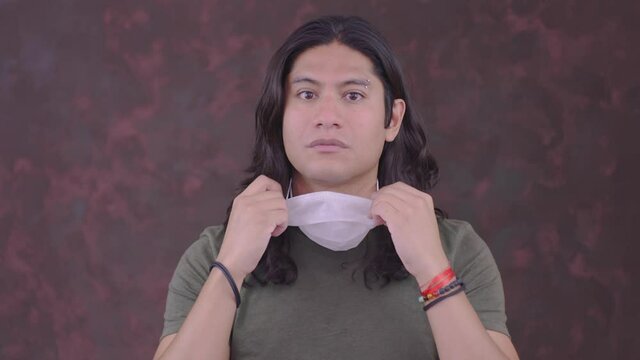chico e hispano y bien parecido mostrando c&oacute;mo quitar y colocar el cubrebocas en esta emergencia sanitaria o pandemia