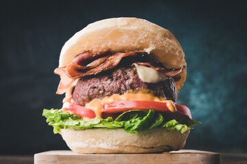 View of fresh tasty burger on wooden table. Hamburger with bacon, cheese, lettuce, tomato and sauce