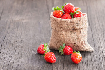 Fresh ripe harvested strawberries in burlap sack on wooden table, Garden summer fruit, strawberry, copy space ( Fragaria )