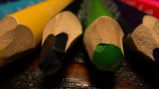 Many colored pencils lie in row. Sliding over pencils on table. Macro shot on laowa lens.