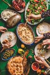 Family having Turkish dinner. Flat-lay of people hands over table with lamb in yogurt sauce, fresh arugula and strawberry salad, rice pilav and flatbread, top view. Ramazan iftar supper, celebration