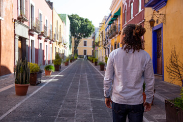 Man with curly hair, walking on colorful colonial street of Puebla