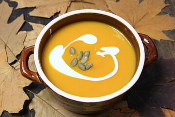 Zupa krem z dyni w kamionkowym naczyniu otoczona brązowymi liśćmi