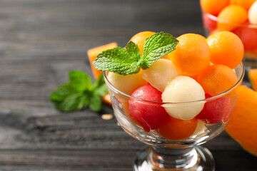 Melon and watermelon balls with mint in dessert bowl on black wooden table, closeup. Space for text