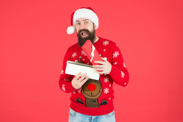 happy bearded male wearing funny knitted sweater and santa claus hat and open present box has an idea for celebrating xmas party, xmas shopping