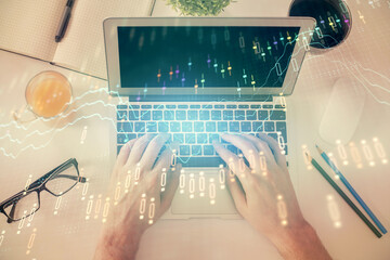 Double exposure of man's hands typing over laptop keyboard and forex chart hologram drawing. Top view. Financial markets concept.